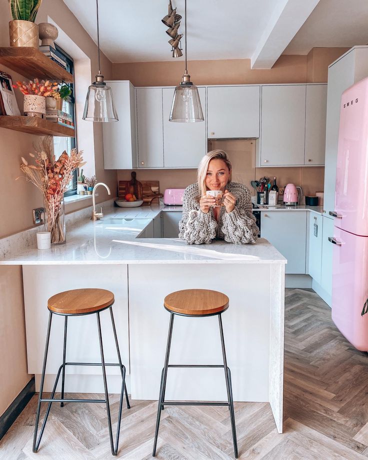 a woman sitting at a kitchen counter drinking from a cup with two stools in front of her