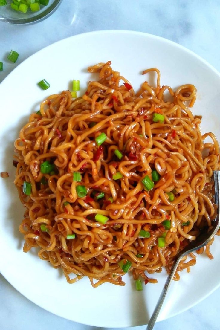 a white plate topped with noodles covered in sauce and green onions next to a fork