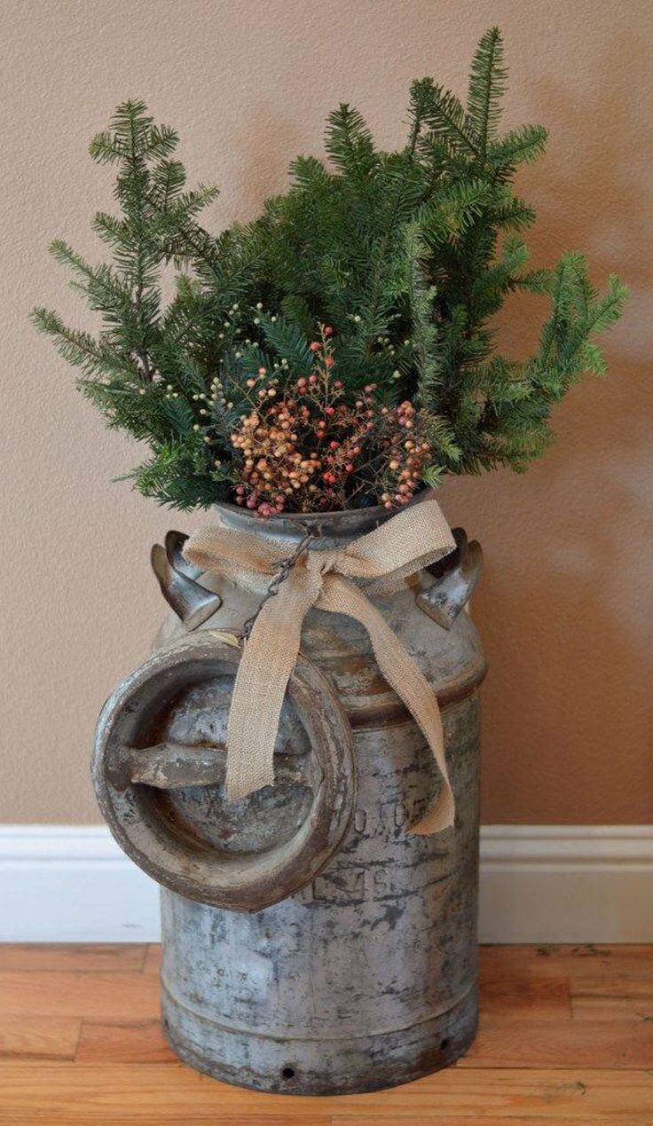 a potted plant in an old watering can with a bow on the handle and pine cones