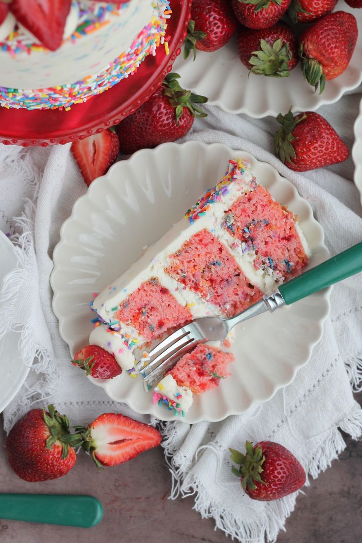 a slice of strawberry cake with sprinkles and strawberries on the side