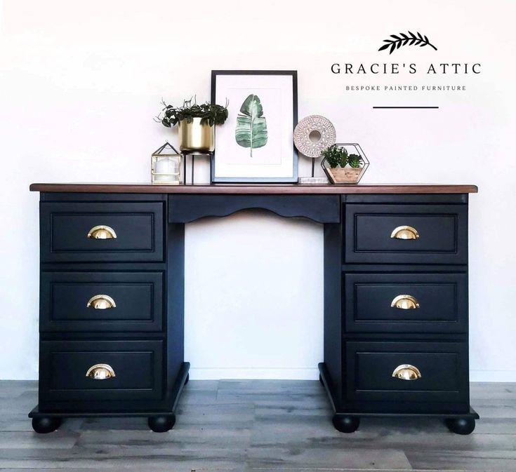 a black desk with two drawers and gold pulls on the top, in front of a white wall