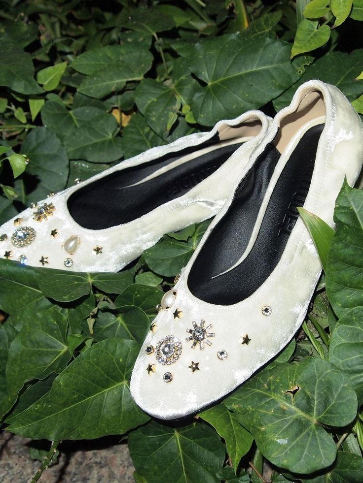 two pairs of white ballet shoes sitting on top of some green leafy plants and leaves