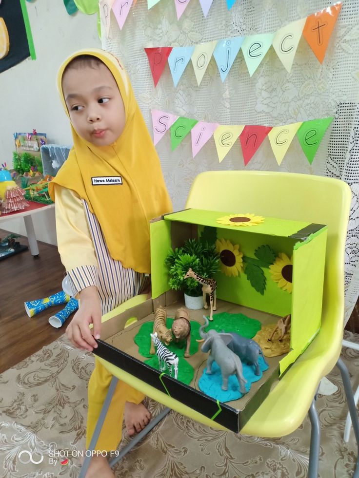 a little boy that is sitting in a chair with some toy animals on the table