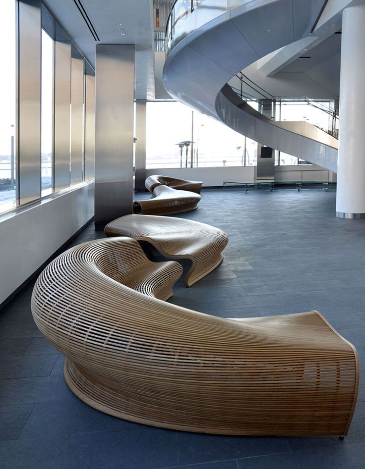 a curved wooden bench sitting in front of a window next to a spiral stair case