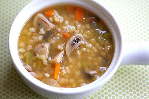 a white bowl filled with soup sitting on top of a green tablecloth next to a spoon