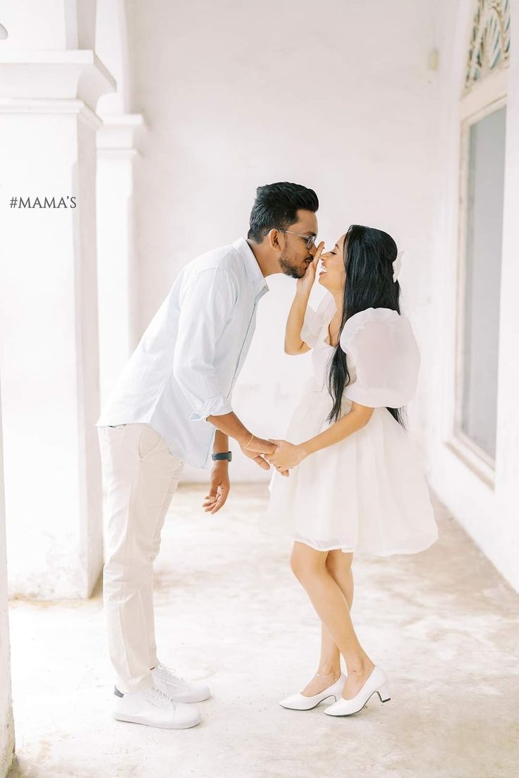 a man and woman kissing each other while standing in front of a white building with windows