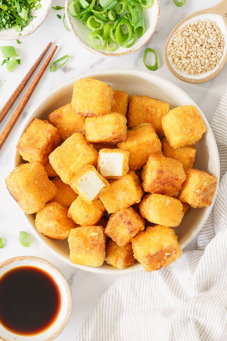 a bowl filled with fried tofu next to chopsticks and bowls of sauce