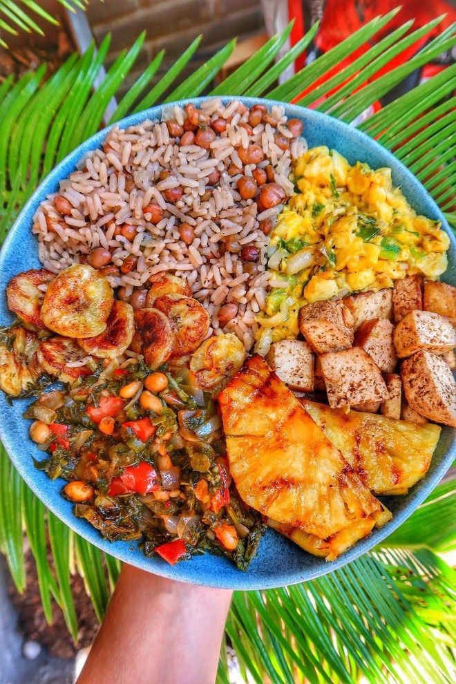 a blue plate topped with rice, meat and veggies next to palm trees