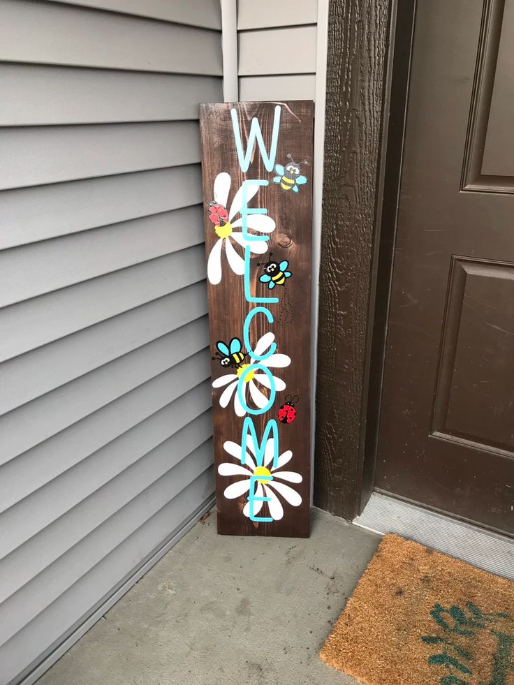 a wooden sign that says welcome with daisies on the bottom and flowers painted on it