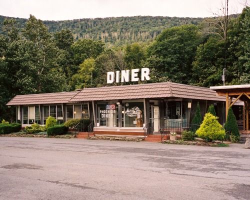 an old diner sits in the middle of a parking lot next to a wooded area