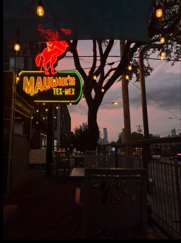 a neon sign for a restaurant on the side of a building at night with lights hanging from it's roof