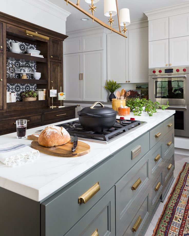 a kitchen with white cabinets and gray counter tops, gold pulls on the doors, an island with a black skillet sitting on it