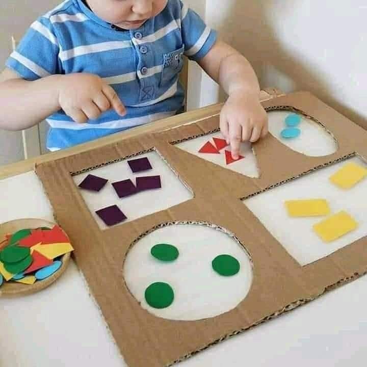 a young boy is playing with some construction paper and magnets on a cardboard board