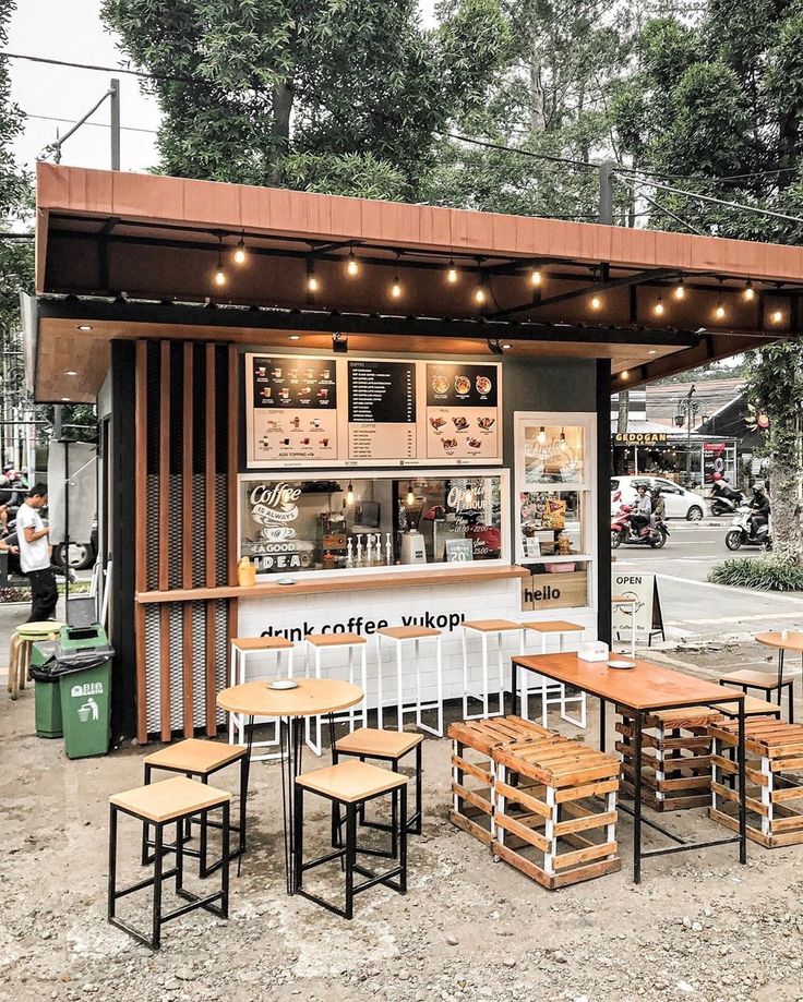 an outdoor coffee shop with wooden tables and stools on the ground, surrounded by trees