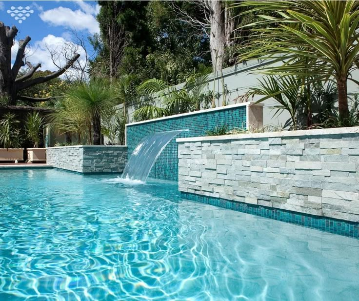 an outdoor swimming pool surrounded by trees and water features a waterfall that runs down the side of it