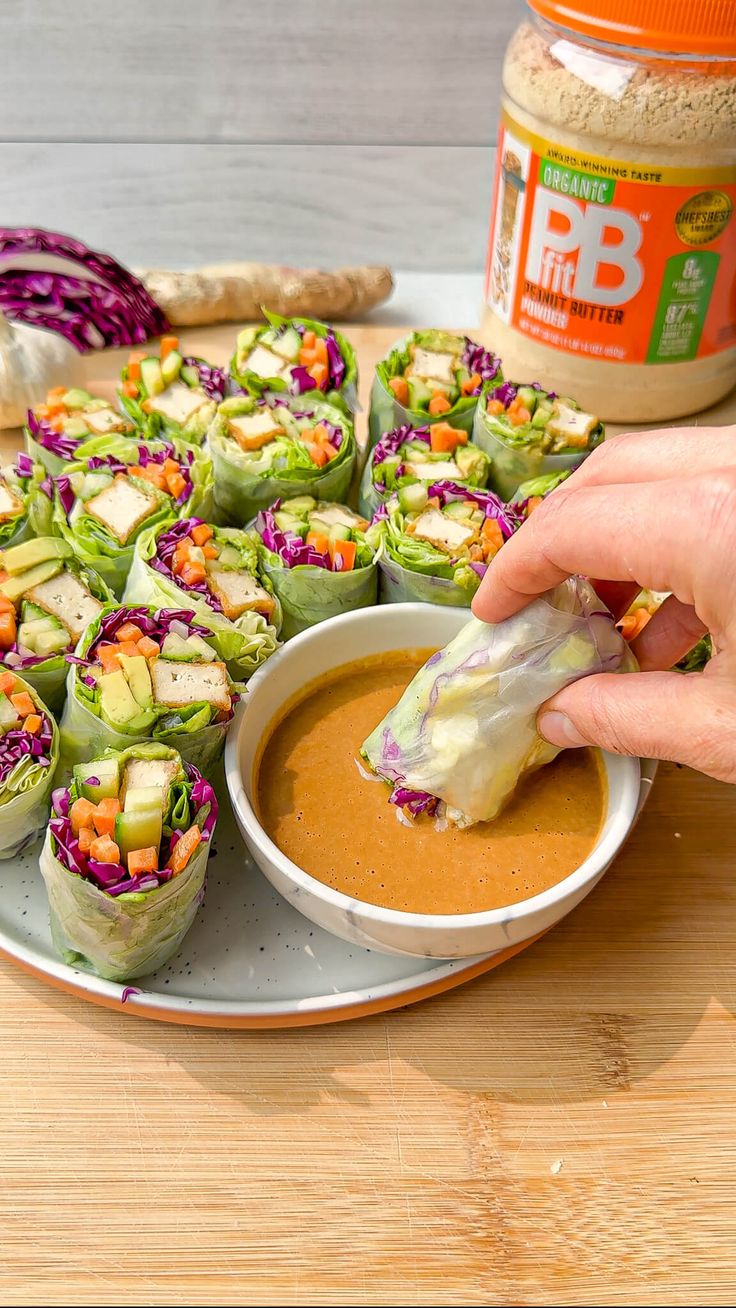 a person dipping some kind of vegetable roll into a bowl with peanut butter on the side