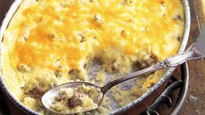 a casserole dish with meat and cheese in it on a wooden table next to a spoon