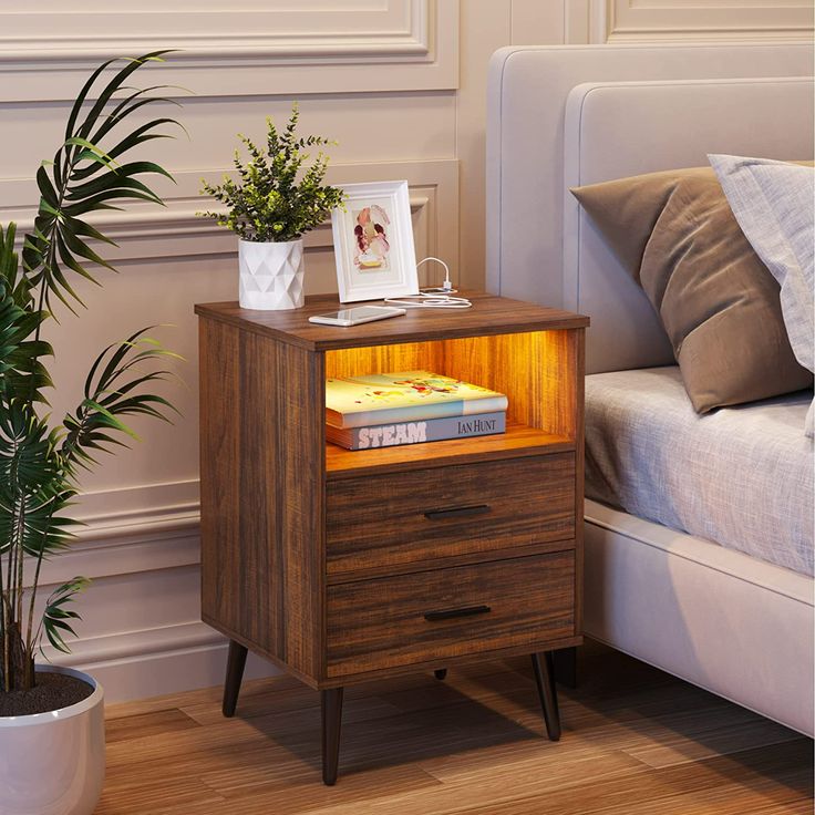 a night stand with a book on it next to a bed and potted plant