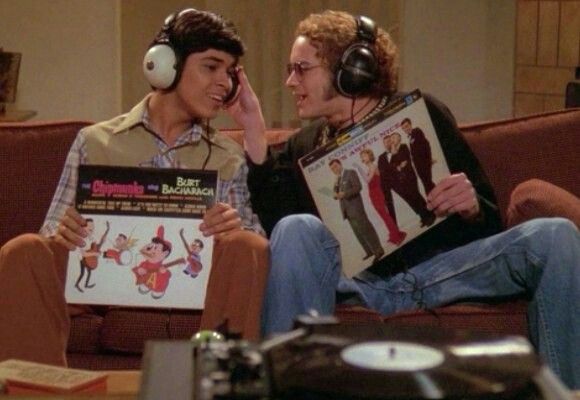 two young men sitting on a couch with headphones and record players in front of them