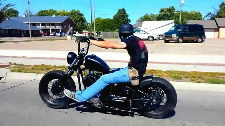 a man riding on the back of a motorcycle down a street next to a parking lot