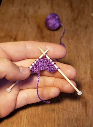 someone is knitting on a wooden table with two skewers next to the yarn