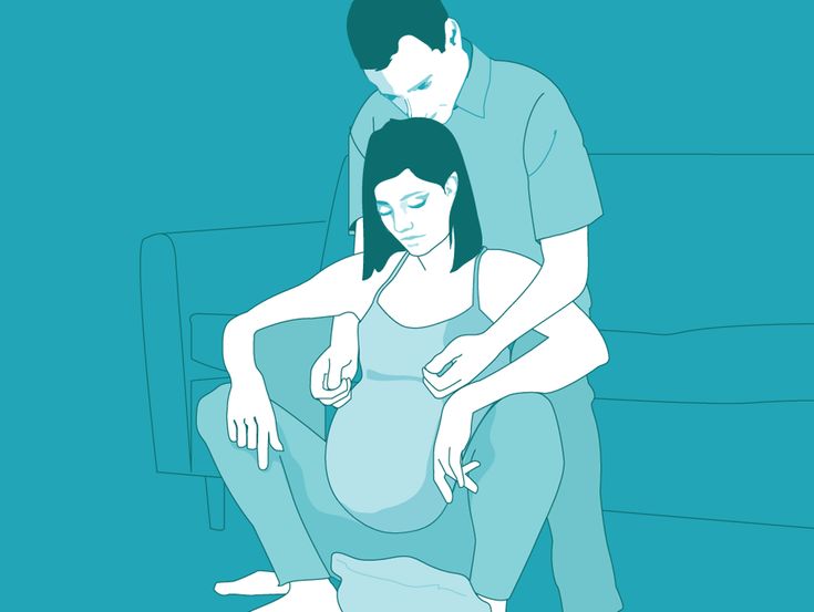 a man and woman sitting on a couch with their arms around each other's pregnant belly