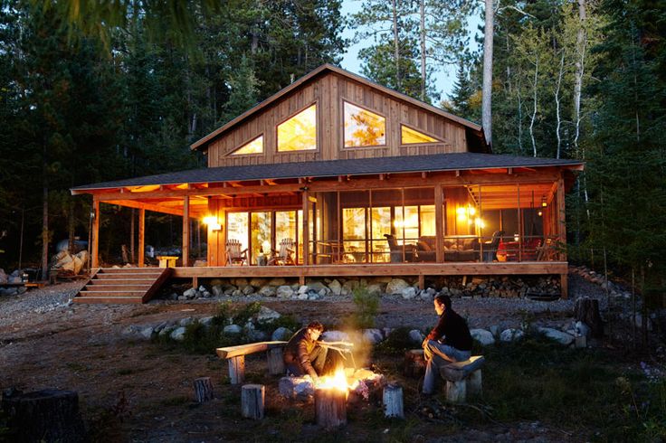 two people sitting around a campfire in front of a cabin