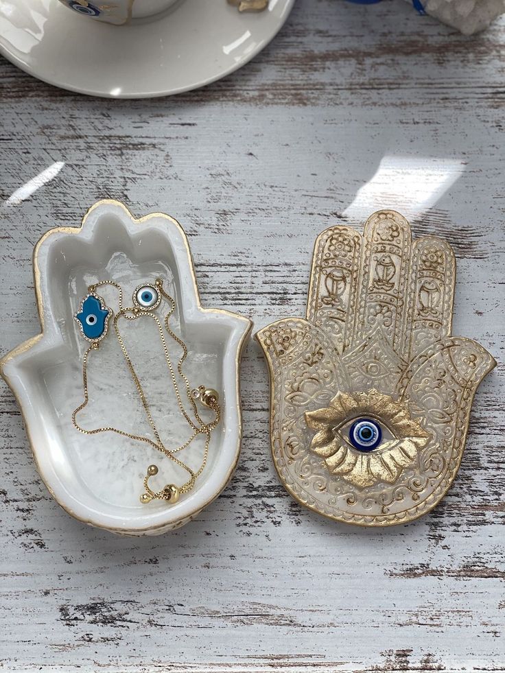 two hamsah shaped dishes with evil eyes on them and one holding an eye