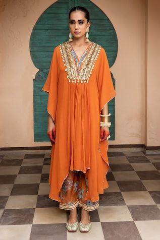 Saffron orange kaftan embellished with mirror, cowrie shells, sequin, resham, dori, pearl and metal coins on the yoke. Paired with floral print pant and slip. - Aza Fashions Kaftan Designs For Ladies, Ritu Kumar Dress, Kaftan Styles For Ladies, Georgette Kaftan, Georgette Kurtis, Kaftan Set, Saffron Orange, Kaftan Styles, Pakistan Dress