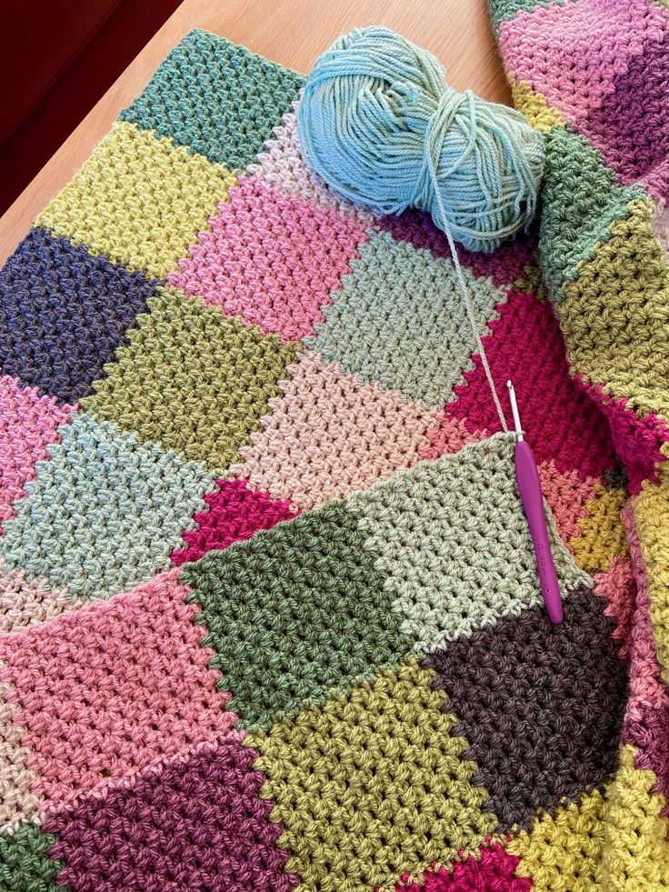 a crocheted blanket with yarn on it and a ball of knitting needles next to it