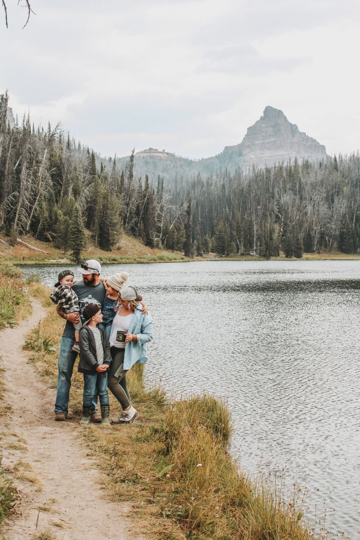 a group of people standing on the side of a lake with mountains in the background