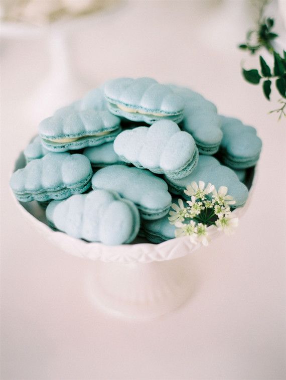 a white bowl filled with blue and green macaroons next to a small flower