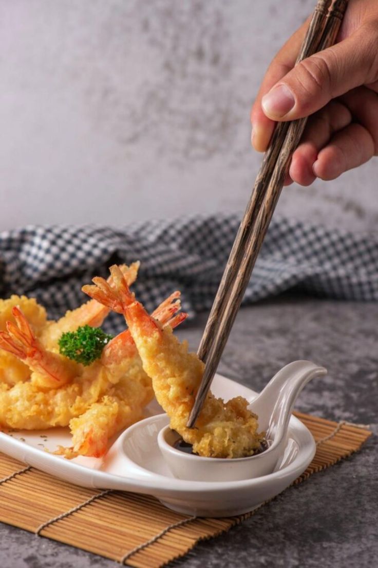 a person holding chopsticks over some food on a white plate with green garnish