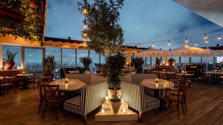 an outdoor restaurant with tables and umbrellas overlooking the city lights at night, lit up by candles