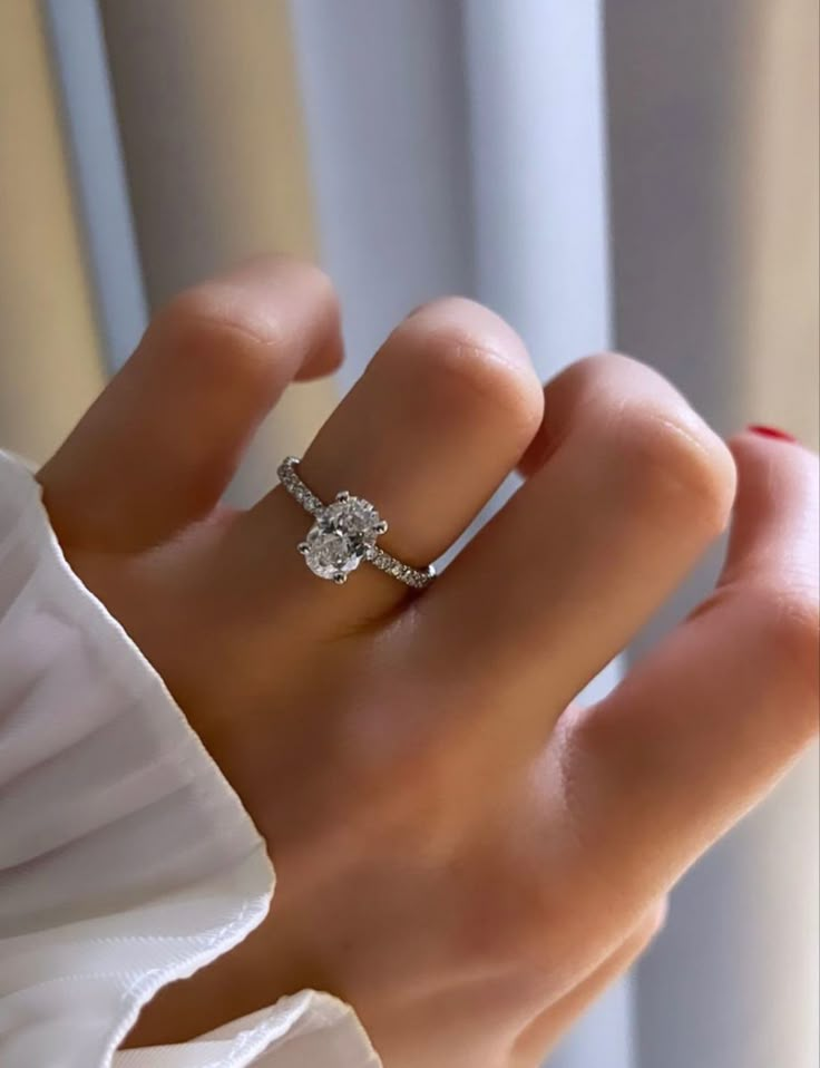 a woman's hand with a diamond ring on top of her finger, in front of a window