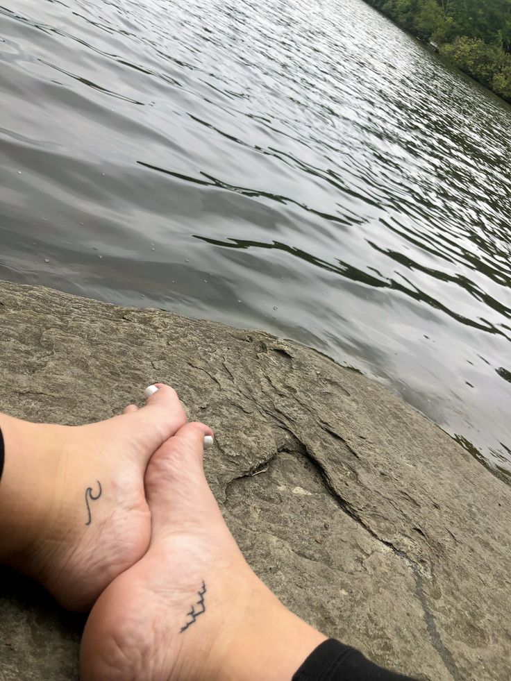 a person sitting on top of a rock next to a body of water with trees in the background