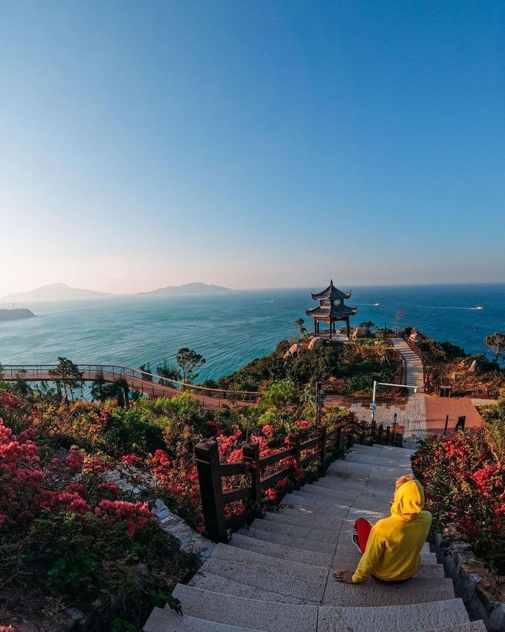 a person in a yellow raincoat is sitting on some steps near the ocean and mountains