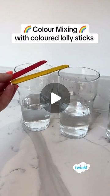 a person holding a pair of colored pencils in front of three glasses filled with water