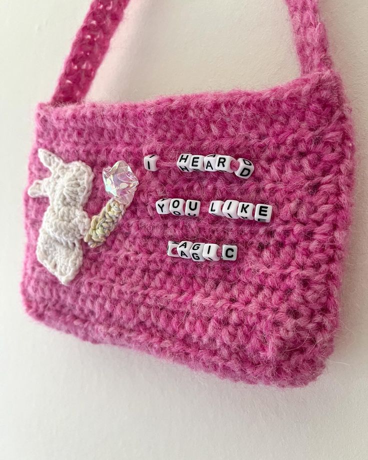 a pink crocheted purse with words written on the side and a small white sheep