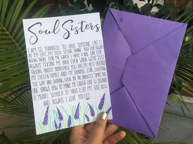 a hand holding up a purple envelope with the words soul sisters written on it, next to a plant