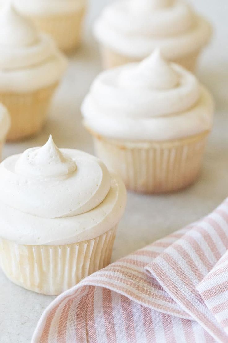 several cupcakes with white frosting on top and pink stripped napkin next to them