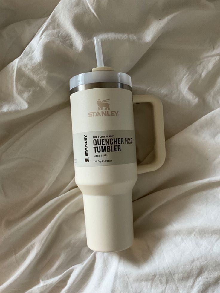 a white coffee cup sitting on top of a bed next to a bottle with a straw in it