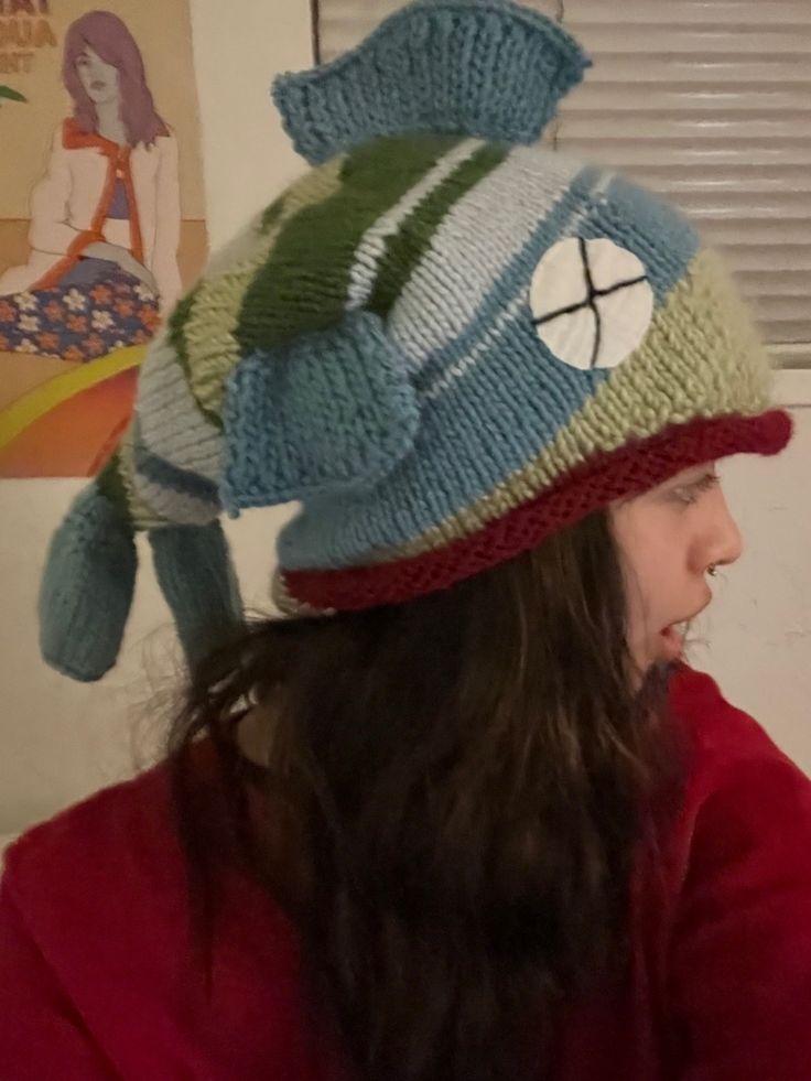 a woman wearing a knitted hat with a fish on it's side, in front of a window