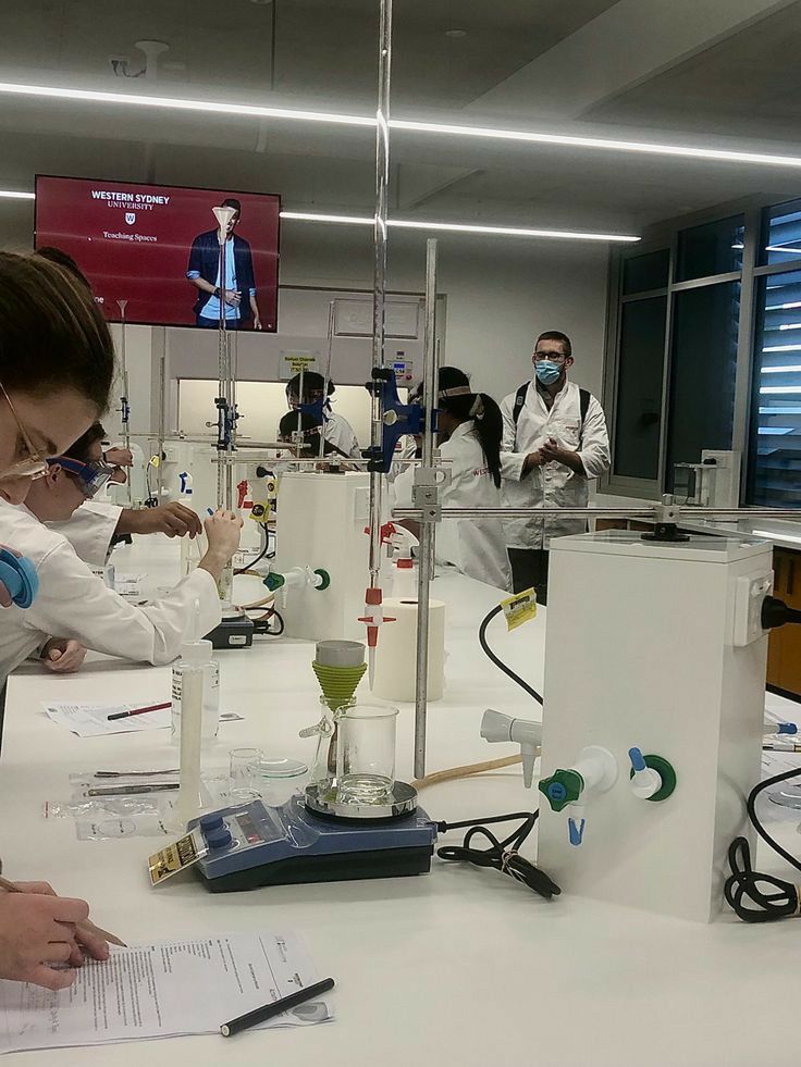 people in lab coats working with equipment on a white table and two men standing behind them