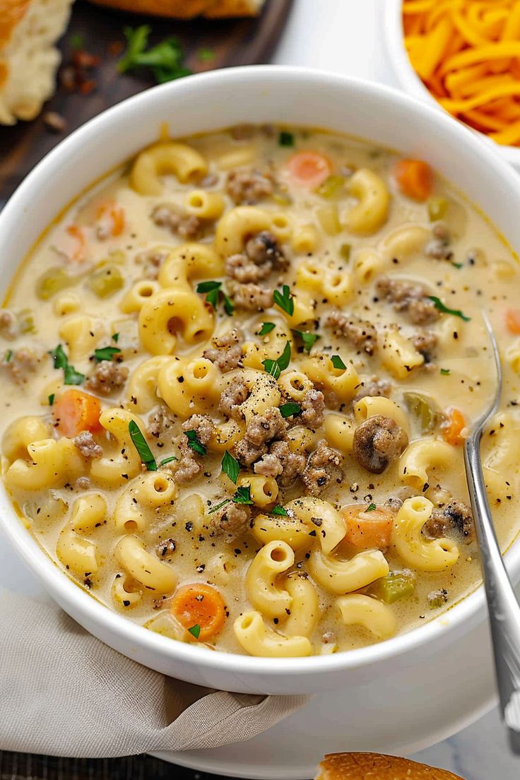 a white bowl filled with pasta and meat soup next to bread on a wooden table