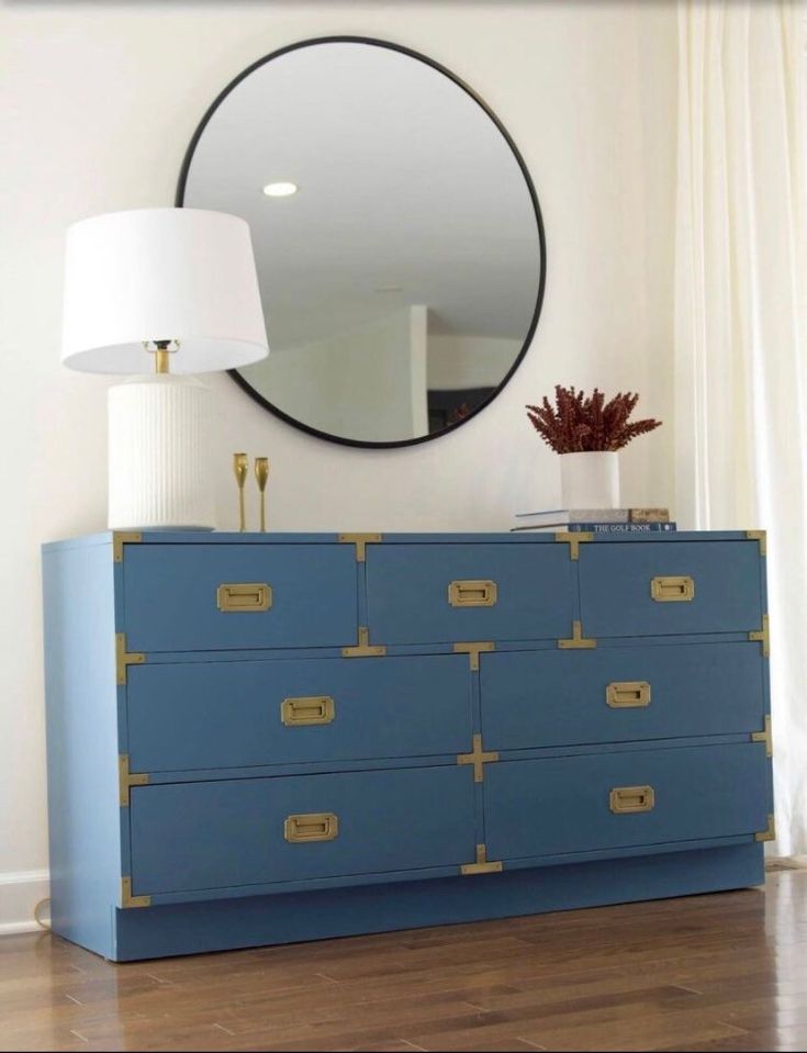 a blue dresser sitting in front of a round mirror