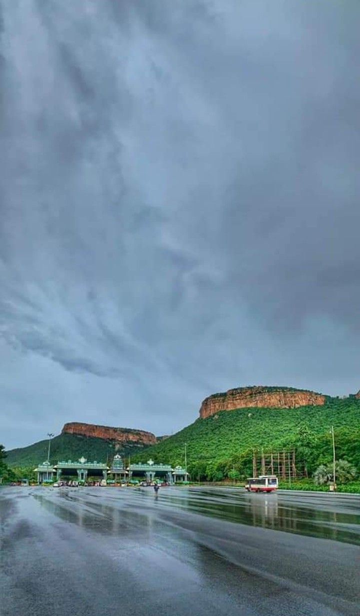 boats are parked on the wet beach in front of some green mountains and trees, under a cloudy sky