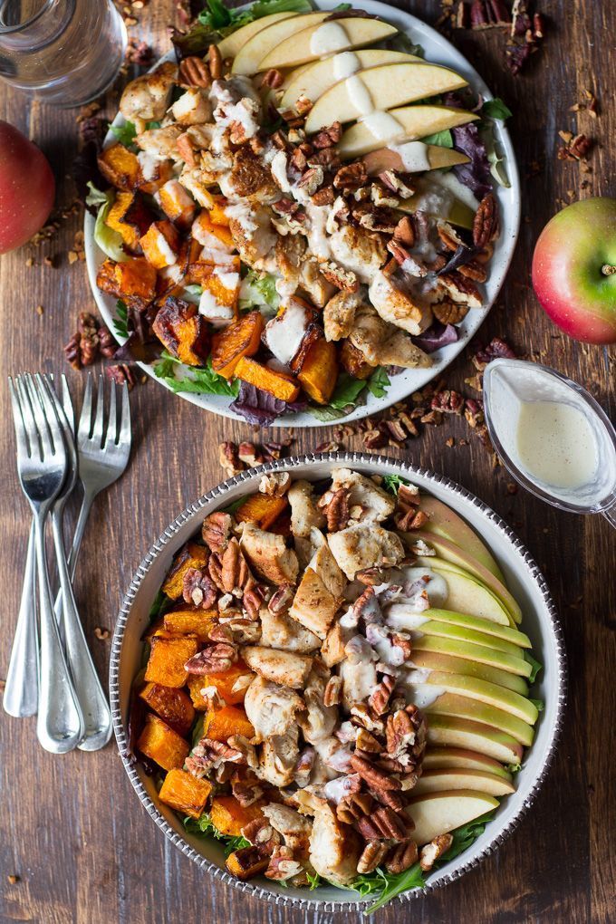 two bowls filled with salad and fruit on top of a wooden table next to silverware