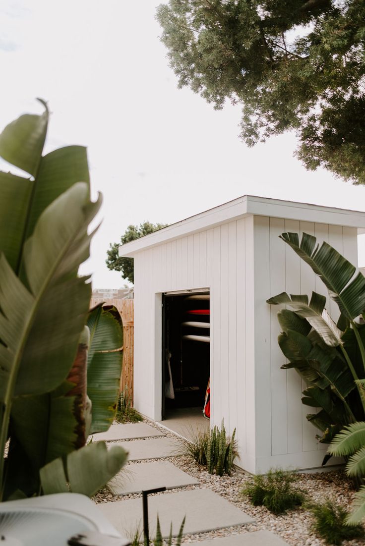 a small white shed sitting next to a lush green tree