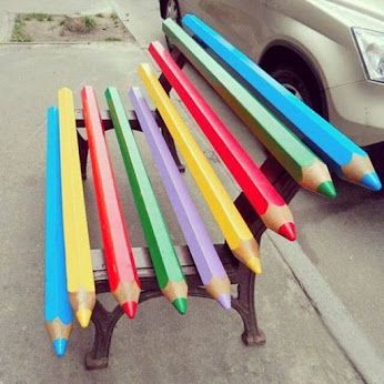 there are many colored pencils sitting on the back of a bench in front of a car